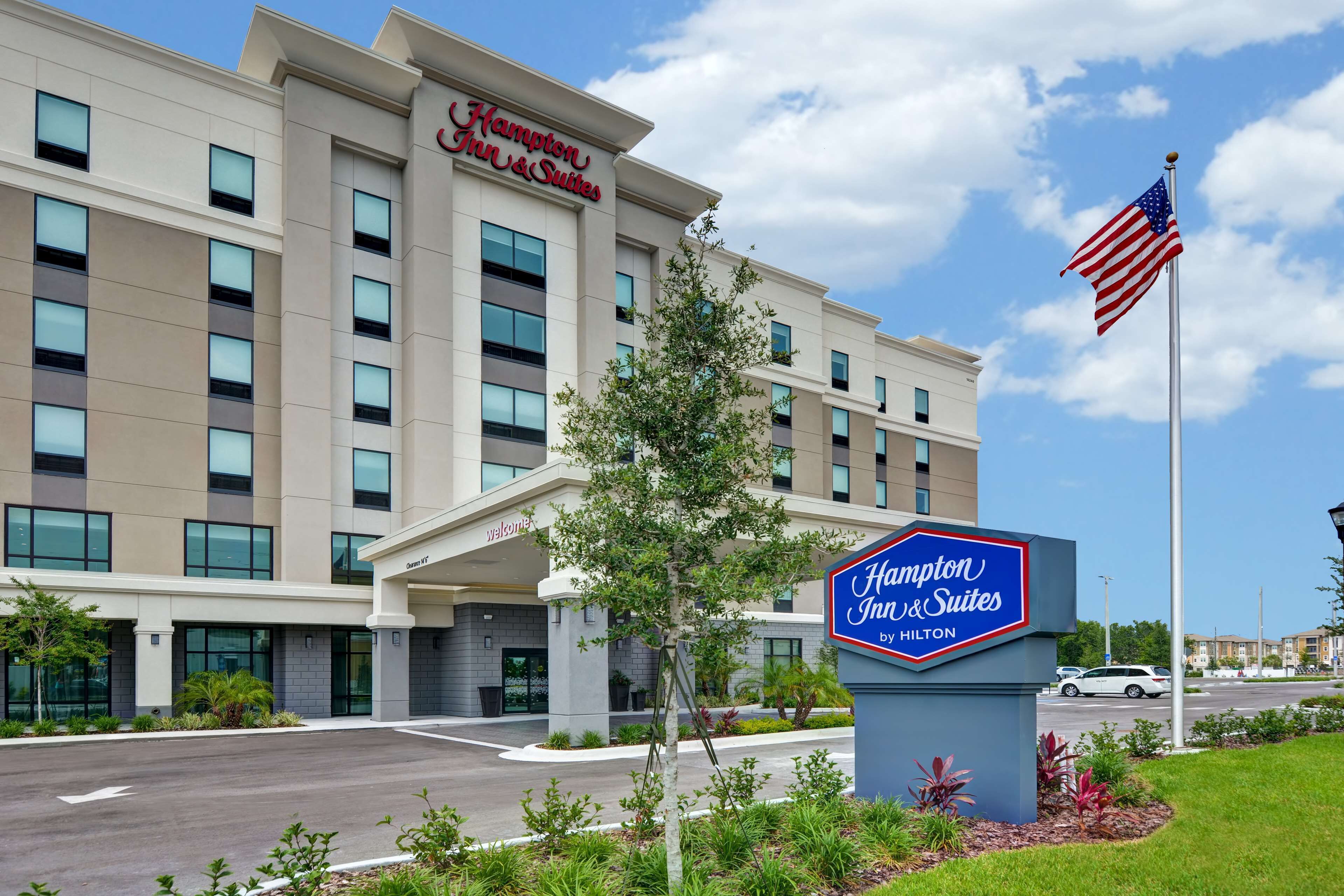 A Hampton Inn & Suites by Hilton building with a clear sky and an American flag.