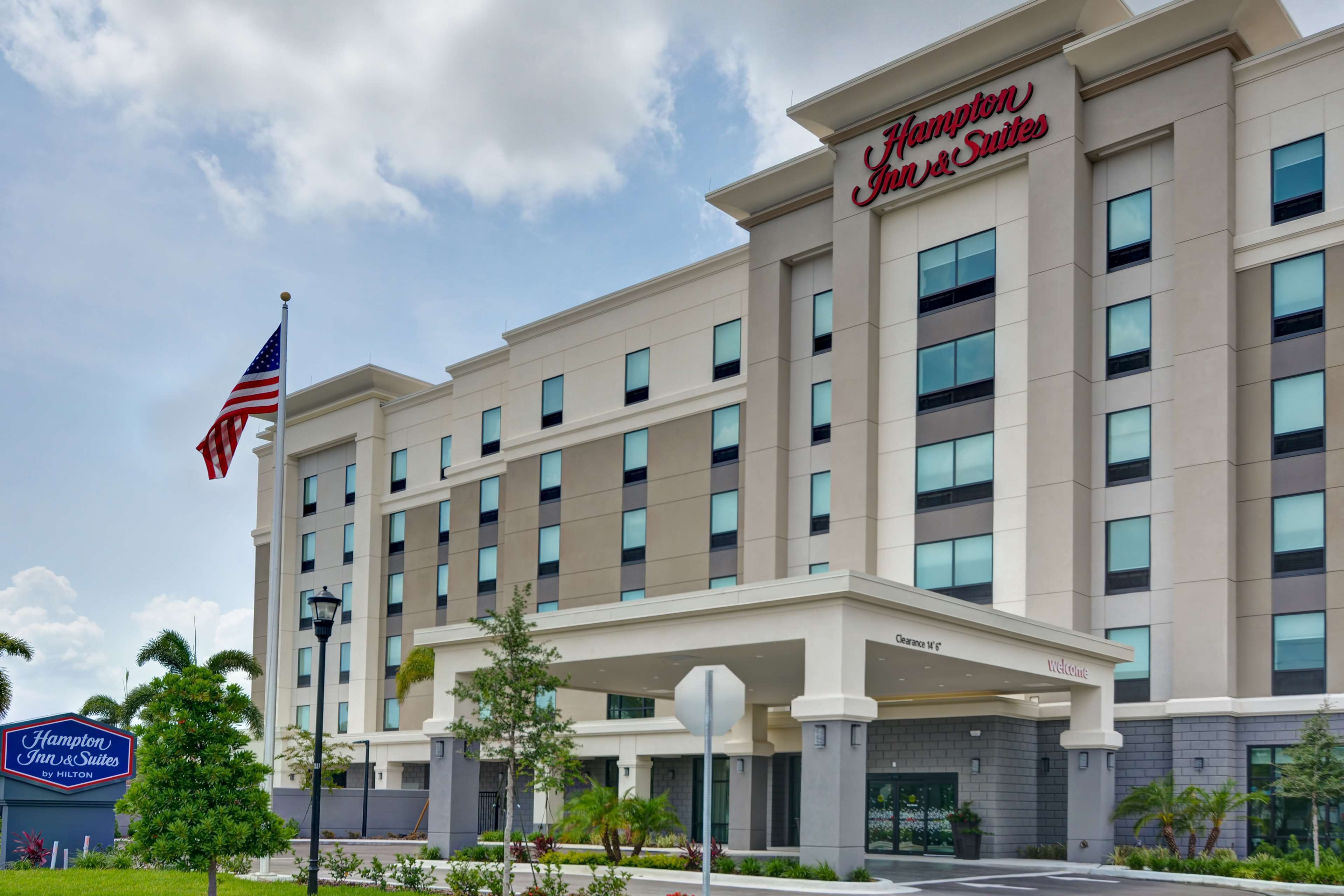 Un bâtiment de la chaîne Hampton Inn & Suites by Hilton, avec un drapeau, une enseigne et une entrée abritée.