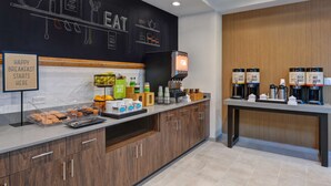 A breakfast area with a chalkboard wall, a coffee station, and a sign indicating breakfast starts here. - Hampton Inn & Suites Tampa Riverview Brandon (Tampa)