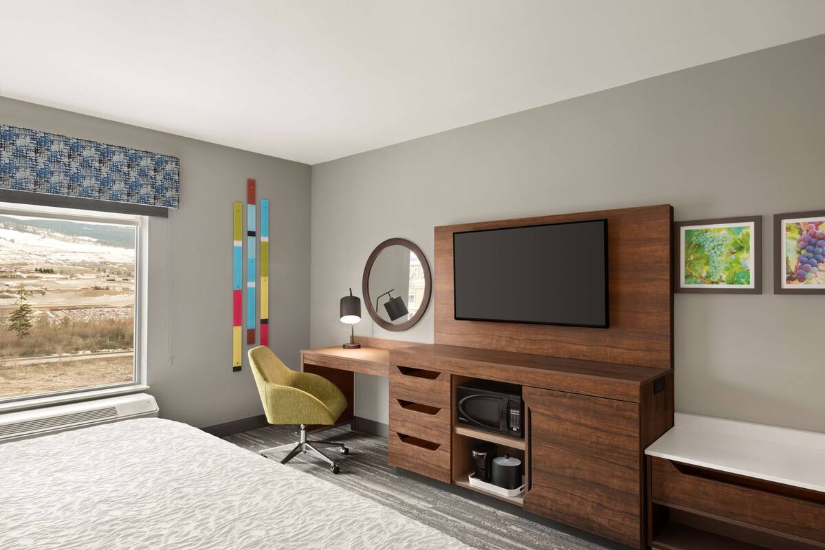 A modern bedroom with a large bed, a desk with a chair, a television, and artwork on the wall.
