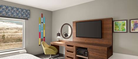 Un dormitorio moderno con una cama grande, un escritorio con silla, televisión y una obra de arte en la pared.