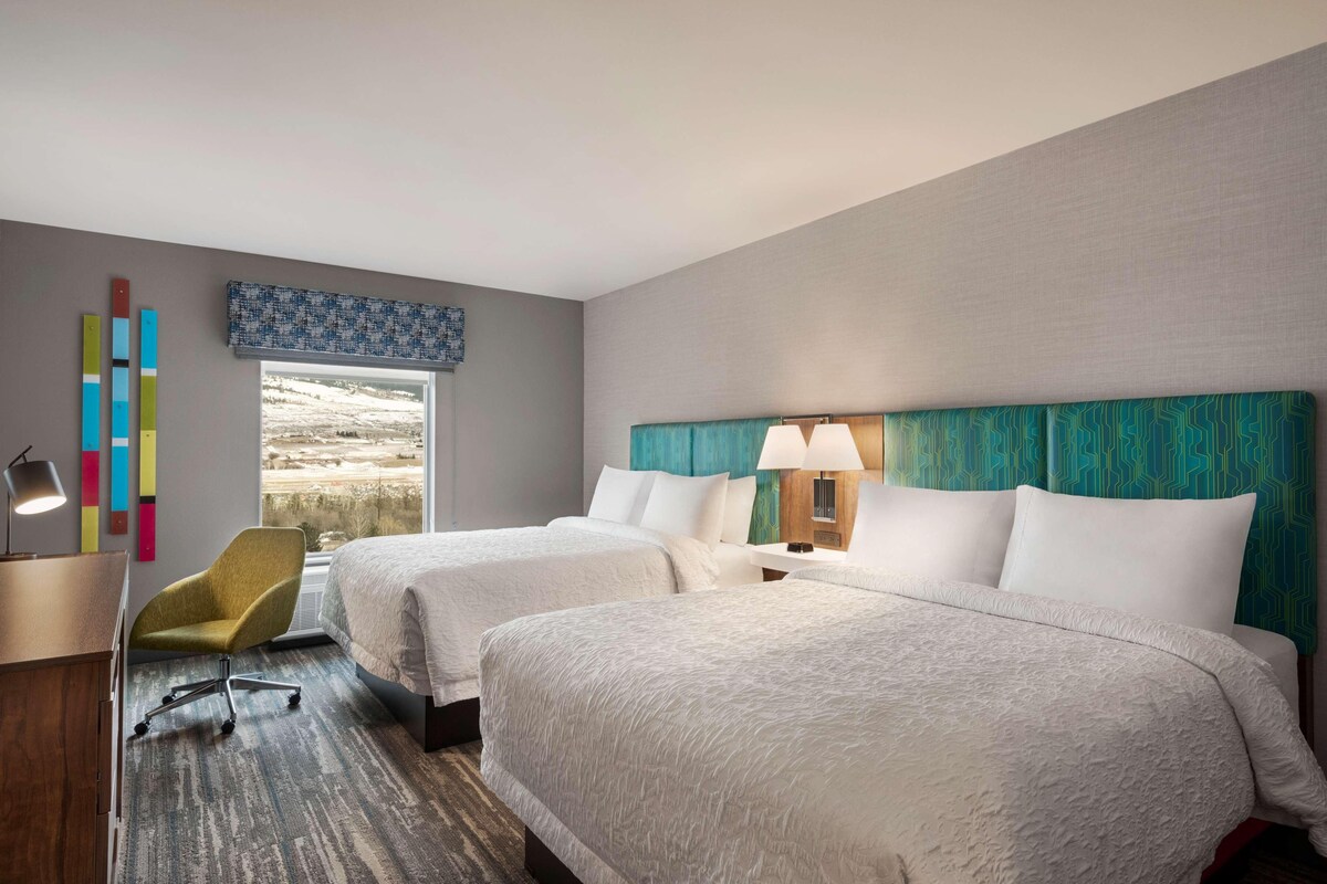 Habitación de hotel con dos camas, un escritorio, una silla y vistas a un paisaje.