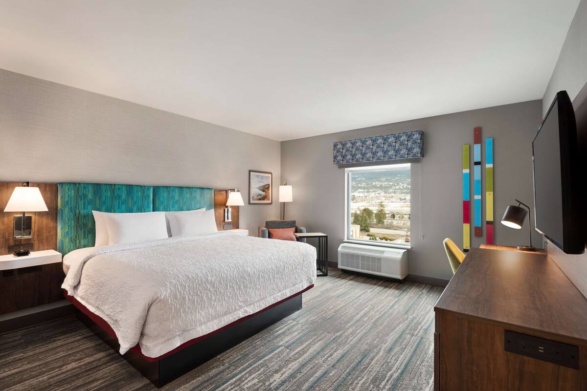 A hotel room with a large bed, a desk, a chair, a window with a city view, and a TV.