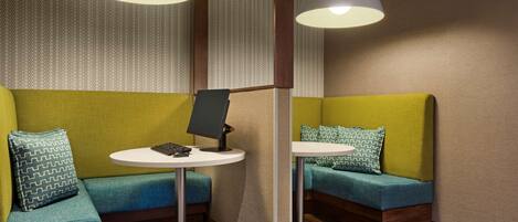 A modern lounge area with green upholstered seating, a small round table with a laptop, and pendant lighting.