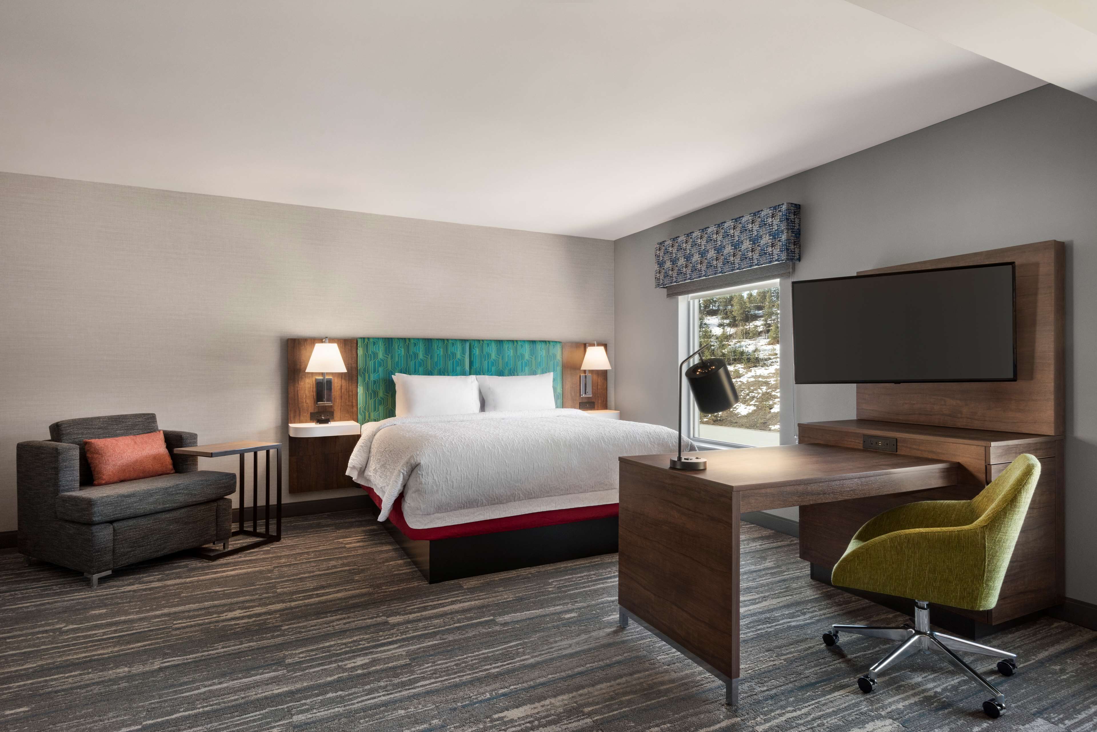 Een moderne hotelkamer met een bed, een bureau, een stoel en een televisie.