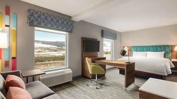Una habitación de hotel moderna con un escritorio, un sofá cómodo, una cama y ventanas amplias que ofrecen vistas al exterior.
