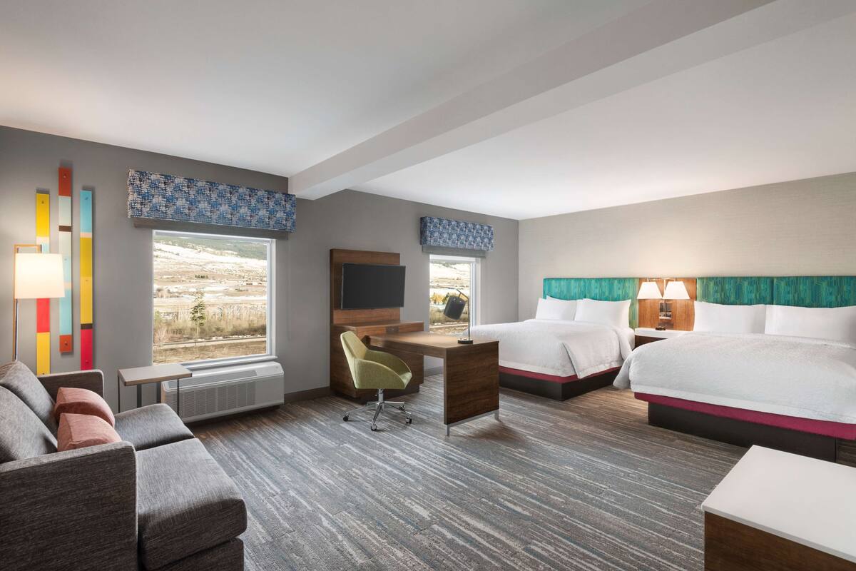 A hotel room with a desk, two beds, a sofa, and a TV.