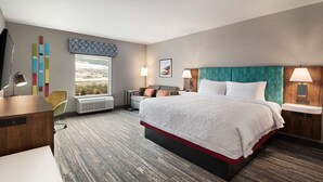 A hotel room with a large bed, a desk, a chair, a window with a view, and a wall with a patterned design. - Hampton Inn & Suites by Hilton Kelowna Airport (Kelowna)