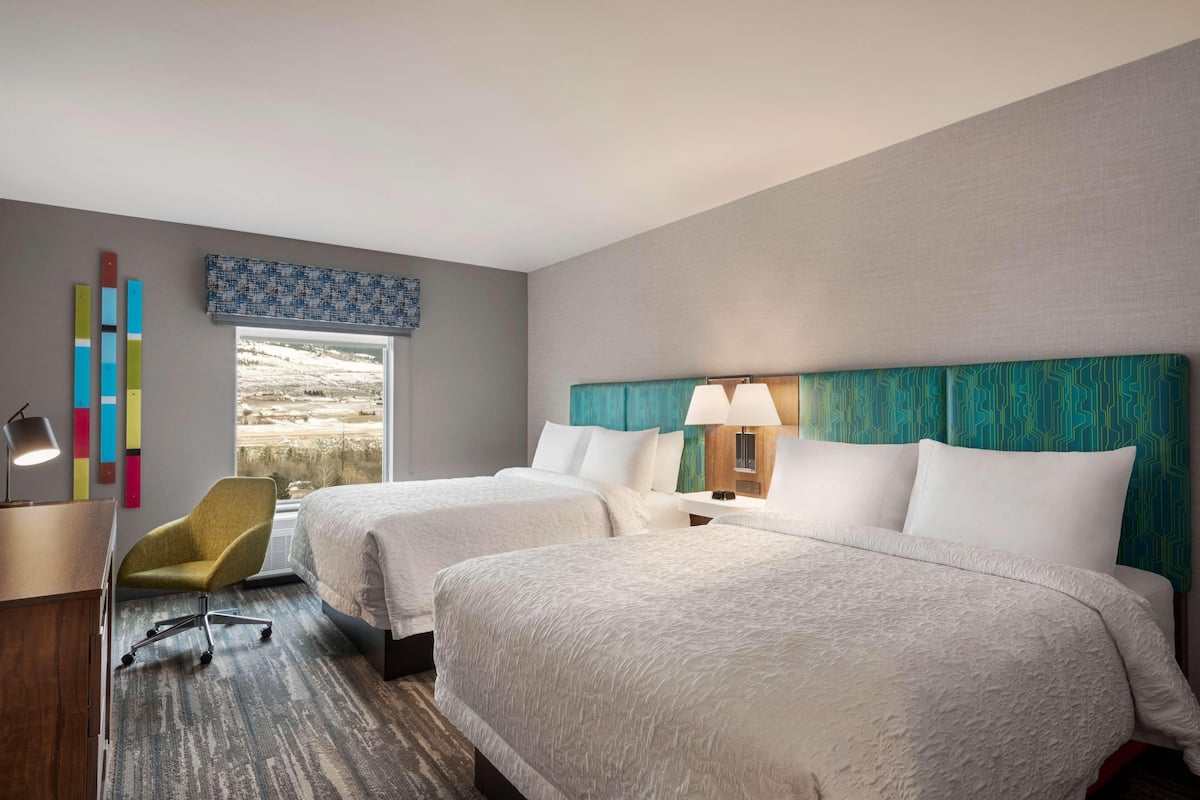 A hotel room with two beds, a desk, a chair, and a view of a landscape.