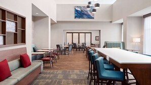 A hotel lobby with a long dining table, multiple chairs, a sofa with red cushions, and a large abstract painting on the wall. - Hampton Inn & Suites by Hilton Kelowna Airport (Kelowna)