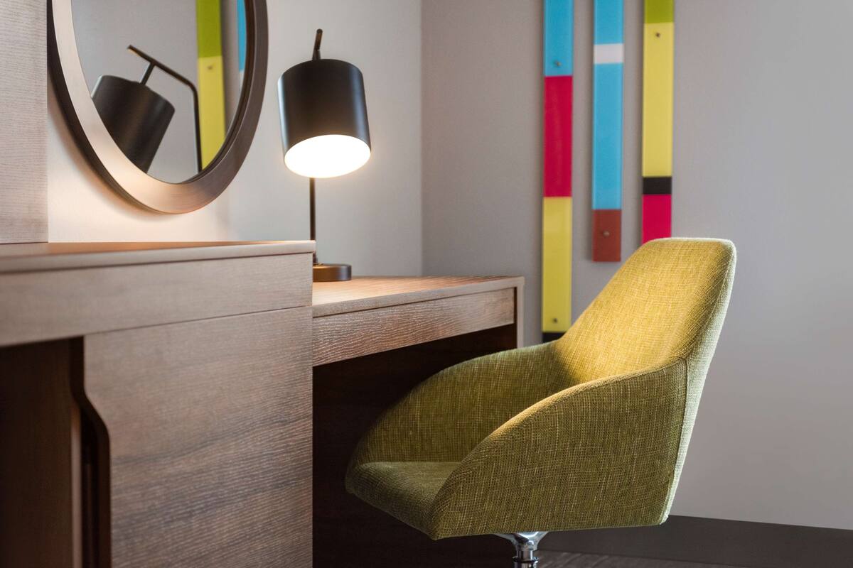 A modern desk with a lamp, a green chair, and a colorful abstract wall art.