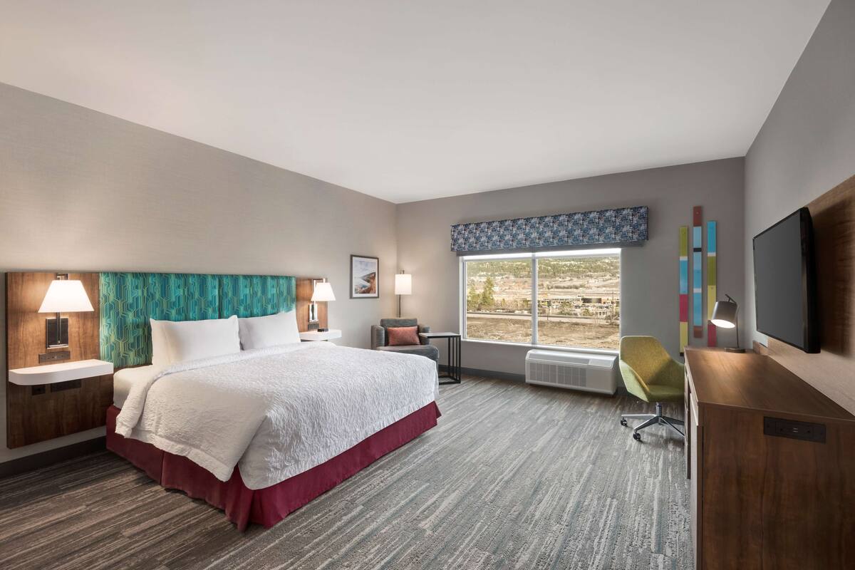 A hotel room with a large bed, a desk, a chair, a TV, and a window with a view of the outdoors.