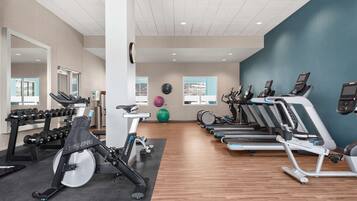 Un gimnasio con equipo cardiovascular, mancuernas y pelotas de ejercicio.