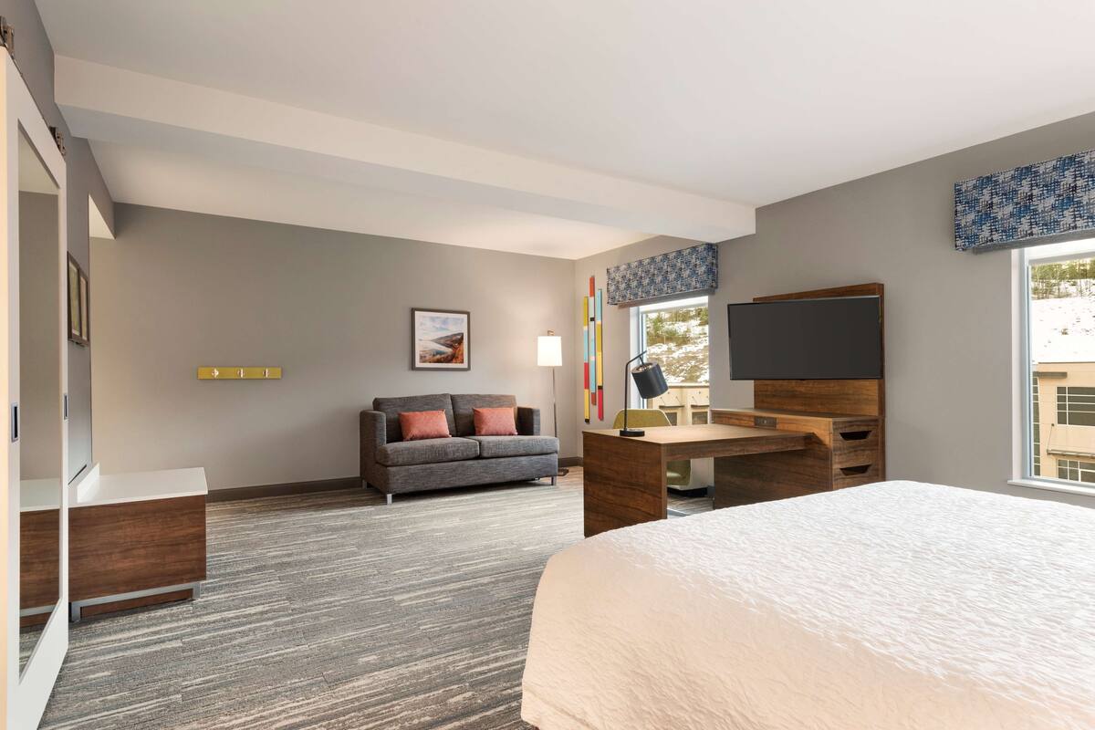 A modern hotel room with a large bed, a desk, a sofa, and a TV.