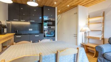 A modern kitchen with dark cabinets, stainless steel appliances, and wooden ceiling.