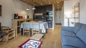 Un salon chaleureux avec un canapé bleu, une table à manger en bois et des chaises. On aperçoit à l’arrière-plan un coin cuisine équipé d’appareils électroménagers modernes.