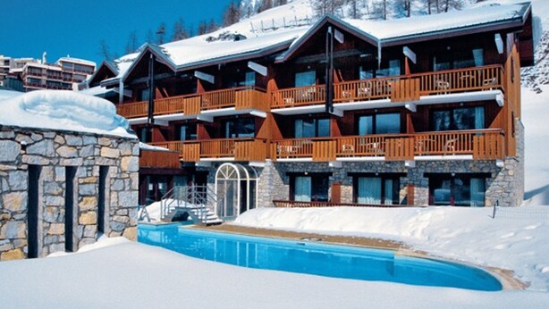 A multi-story lodge with wooden balconies and a stone entrance, surrounded by snow.