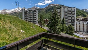 En moderne bygning med balkoner, foran et bjerglandskab og klare himmel.