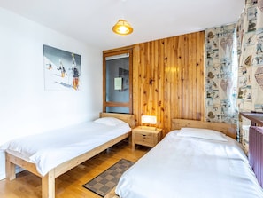 A room with two wooden beds, a wooden wardrobe, a wall-mounted picture, and a patterned curtain.