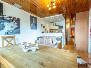 Een gezellige zithoek met een houten plafond, een bank, een eettafel met kaarsen, en een keuken op de achtergrond.