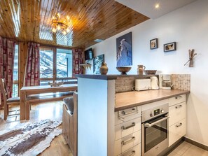 Een moderne keuken met houten kastjes, een ingebouwde oven en een groot raam met uitzicht op een besneeerd landschap.
