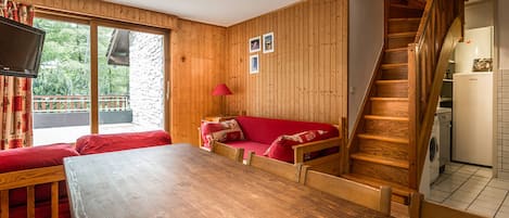 A wooden interior with a sofa, a table, a staircase, and a television.