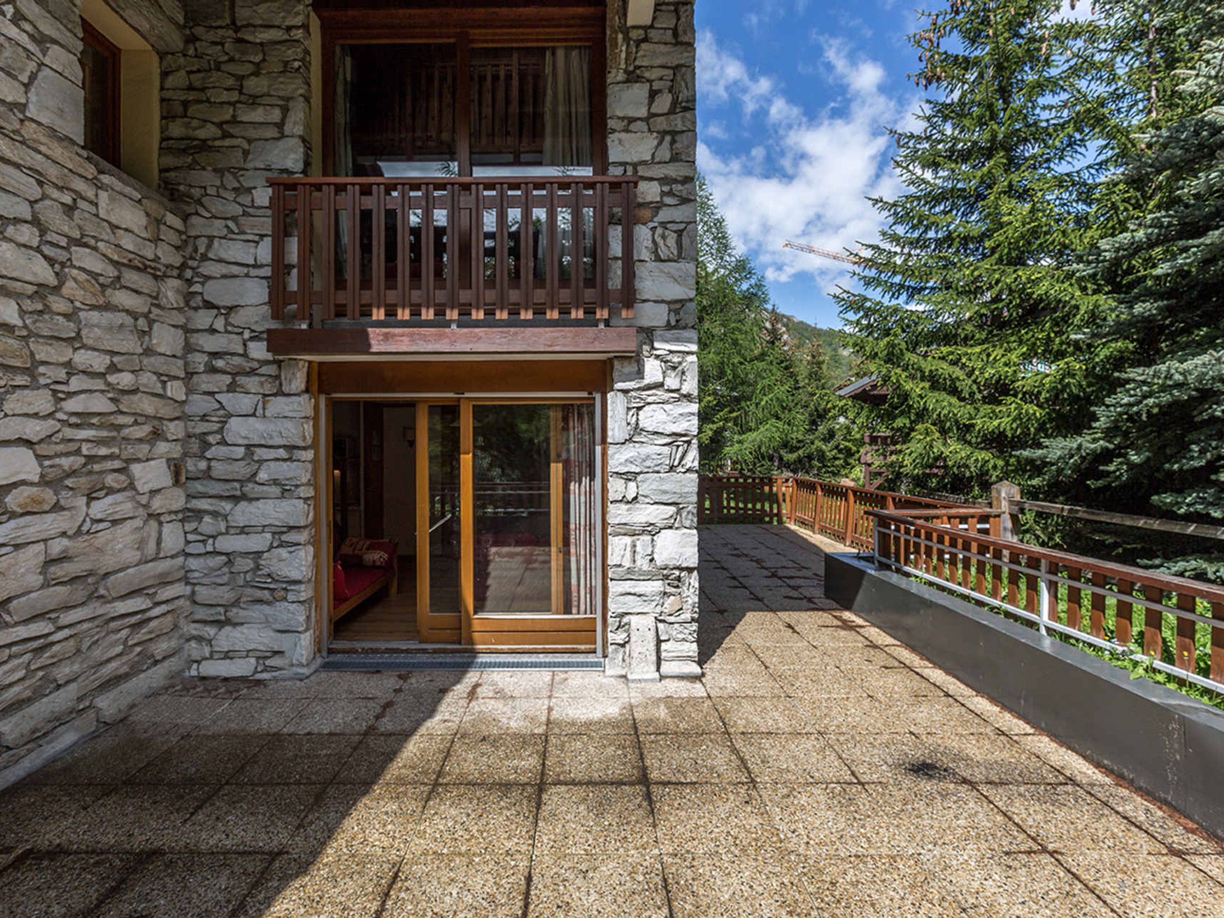 Un bâtiment en pierre doté d’un balcon en bois, d’une porte et offrant une vue sur les arbres.