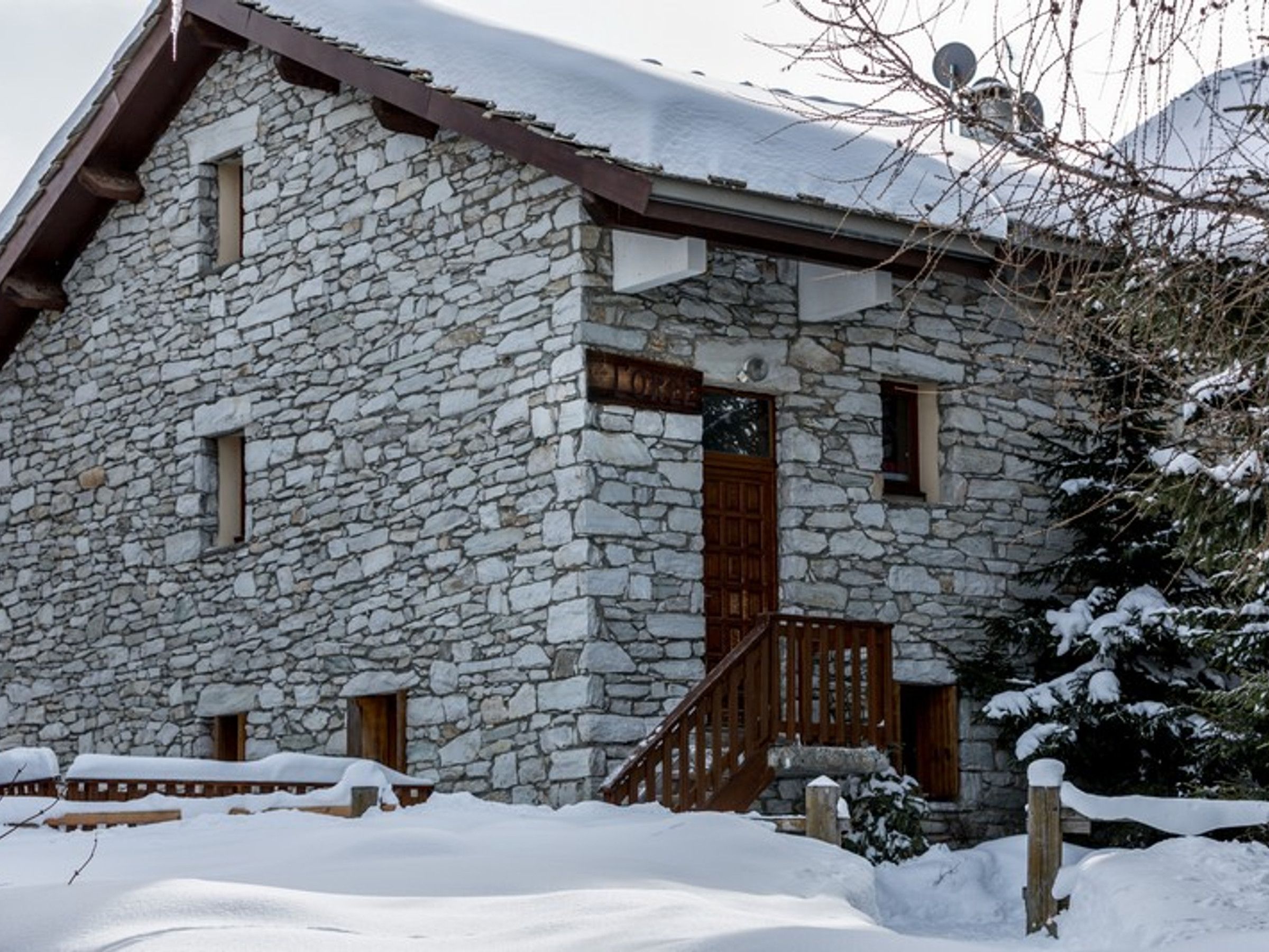 Edificio de piedra con puerta y ventanas de madera, rodeado de nieve.