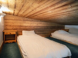 A cozy attic bedroom with two single beds, wooden walls, and a small nightstand.