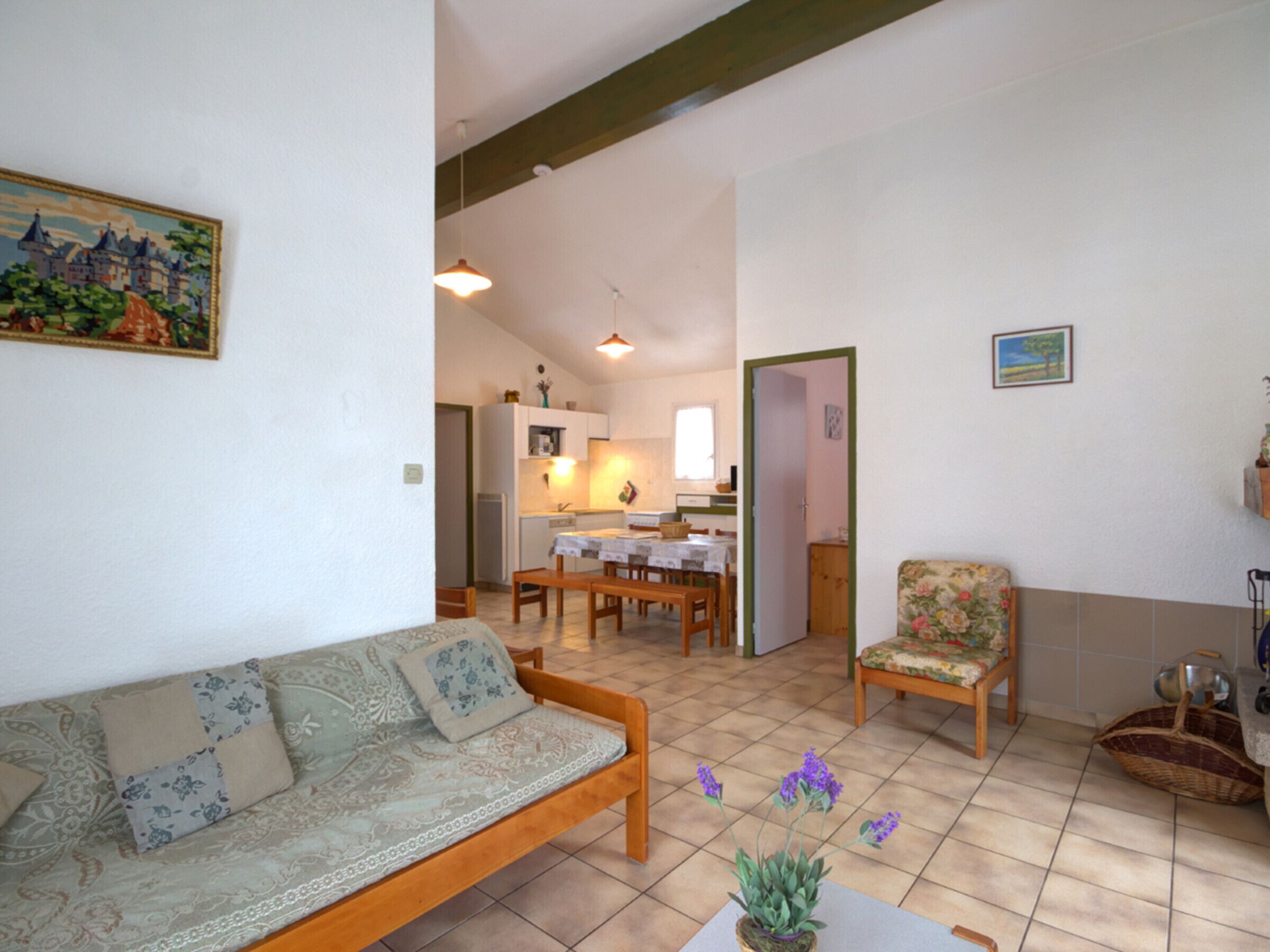 Ein Wohnzimmer mit einer Couch, einem Esstisch mit Stühlen, einer Küche im Hintergrund und einer Tür zu einem anderen Raum.