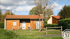 A rustic wooden house with a tiled roof, a wooden fence, and a tree in the background.