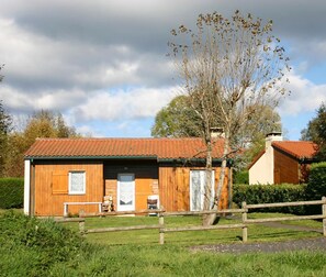 Une maison rustique en bois, avec un toit en tuiles, une clôture en bois et un arbre en arrière-plan.