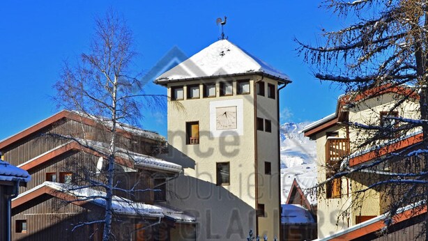 A building with a clock on the tower, surrounded by snow-covered trees and other buildings. - Cozy Studio for 2 with Terrace, Ski-in/Ski-out, Close to Shops - Montchavin La Plagne (La Plagne Montchavin Les Coches)