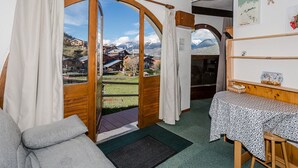 A cozy room with a wooden bench, a small table, and a view of a mountainous landscape through a large arched window. - Cozy Studio for 2 with Terrace, Ski-in/Ski-out, Close to Shops - Montchavin La Plagne (La Plagne Montchavin Les Coches)