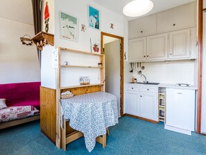 Quarto compacto com cama, mesa pequena, cozinha compacta e estante de madeira.