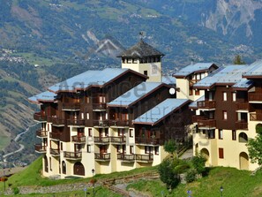 Hotel com vários andares e varandas, com montanhas ao fundo.
