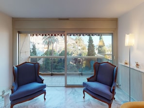 A balcony with a view of palm trees and buildings, two blue armchairs, and a floor with a marble pattern. - Spacious 2P with terrace, garage and wifi in Menton (Menton)