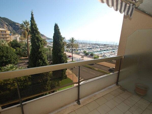 Un balcón con vista a un puerto deportivo, árboles y colinas distantes.
