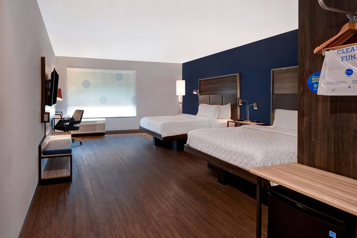 Une chambre d’hôtel avec deux lits, un bureau, une chaise et une fenêtre avec des stores.
