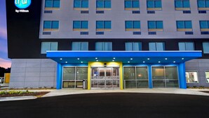 Un hotel de diseño moderno, con un llamativo letrero de 'tru by Hilton', un toldo de entrada azul y una serie de ventanas en la fachada.