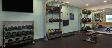 Un gimnasio con racks para pesas, kettelbells y equipo de ejercicio.