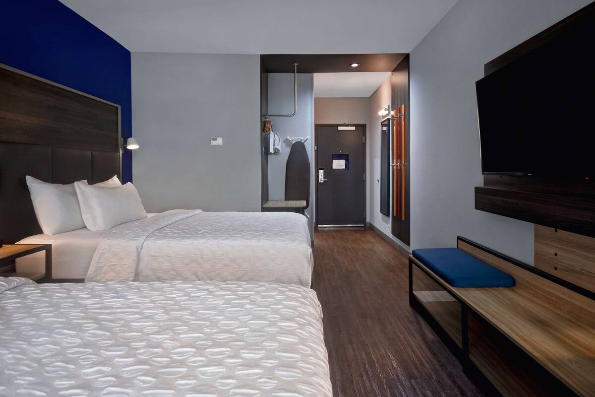 Une chambre d’hôtel avec deux lits, un banc, une télévision et un miroir.