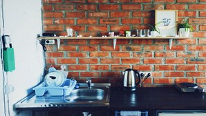 Una cocina con pared de ladrillo, una estantería con utensilios de cocina, una tetera y una cafetera.