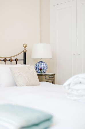A neatly made bed with a white and beige pillow, a blue and white vase with flowers, and a white lamp on a bedside table. - Charming Grand One bedroom (London)