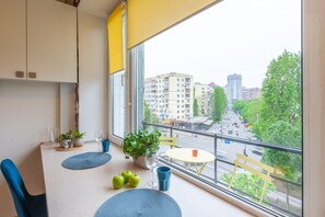 A balcony with a table, chairs, potted plants, and a view of the cityscape.