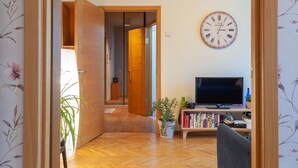 A wooden-framed doorway leading to a living area with a wooden floor, a clock on the wall, a television, and a bookshelf. - MalinaApt Botanical apartment (Kyiv)