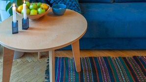A room with a blue sofa, a round wooden table with a bowl of fruit and candles, a large green plant, and framed pictures on the wall. - MalinaApt Botanical apartment (Kyiv)