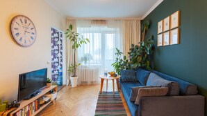 A living room with a TV, books, a clock, and plants. - MalinaApt Botanical apartment (Kyiv)