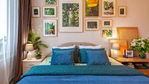 A neatly arranged bedroom with a bed, bedside tables, a nightstand, and a wall adorned with framed botanical prints. - MalinaApt Botanical apartment (Kyiv)