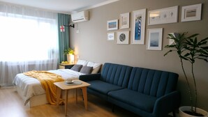A modern living room with a bed, a blue sofa, a small wooden table, and a potted plant. - MalinaApt Sea Place (Kyiv)